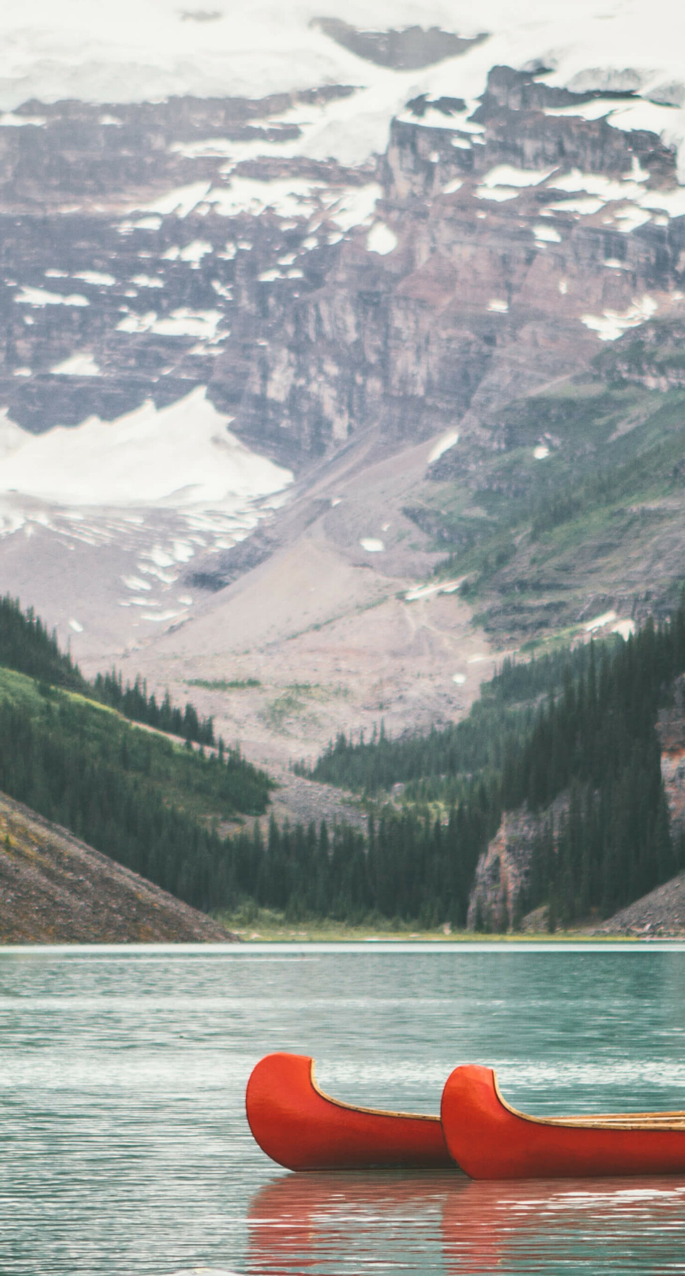 Red canoes in a lake valley between trees and large mountains