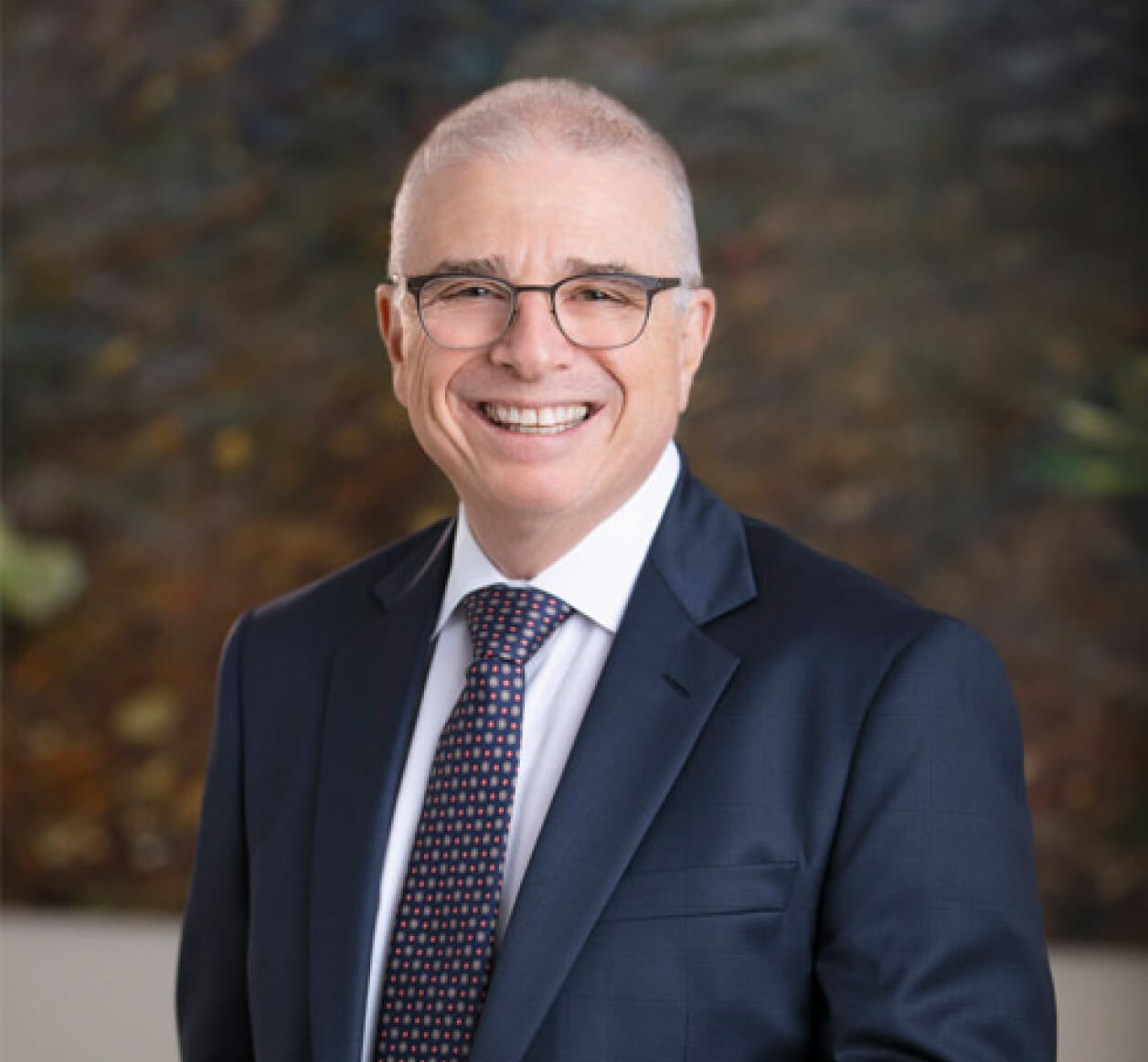 Business man wearing glasses, a blue suit and patterned tie smiling