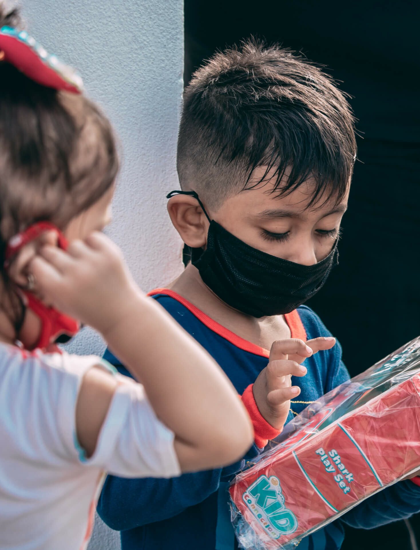 A young boy and girl wearing face masks holding a Shark Play set toy